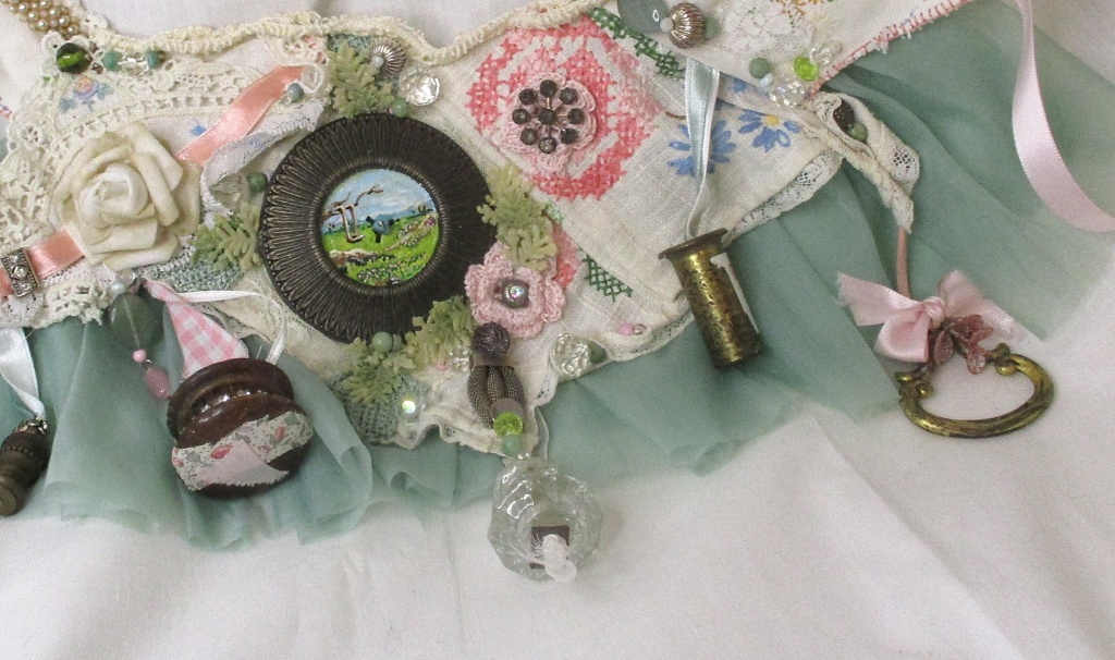 close up center of fairytale sash handmade by Marelle Couture for Hopscotch Couture. This is a multipurpose sash/necklace and is made from antique hardware, findings and vintage jewelry. All hand sewn. https://hopscotchcouture.com/products/large-trinket-bib-necklace-fairytale-princess-sash-neck-piece-antique-assemblage-statement-bib-bridal-necklace #bridalsash #bibneckpiece #handmadebridalaccessory #pastelsash 